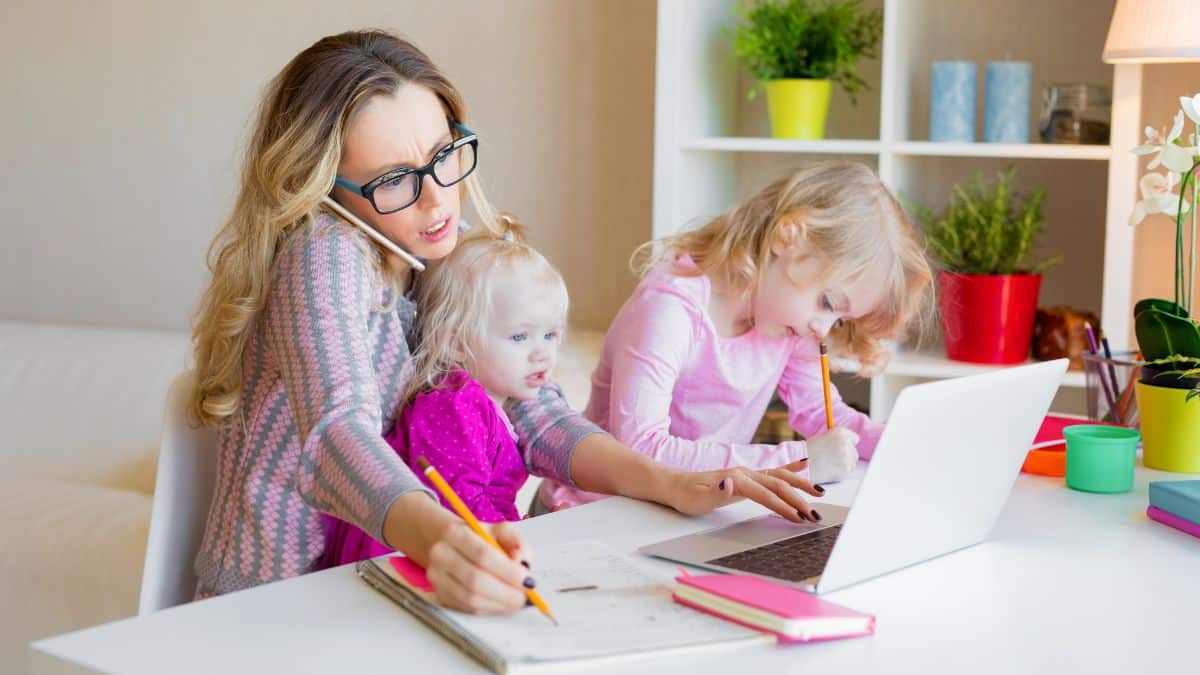 Overwhelmed mom sitting at kitchen table feeling mentally exhausted from daily mental load with her kids